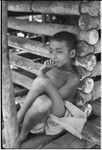 Boy leans against wall of a yam house, with good detail of notched pole construction