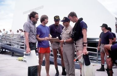 Navy divers from Mobile Diving Salvage Unit One review charts with U.S. Park Service personnel prior to a survey dive. The divers are studying the wreck of the battleship USS ARIZONA (BB-39) as part of Project Sea Mark, a four-year undersea survey and mapping study of naval historic sites. The study is being conducted in conjuction with the U.S. Park Service's Submerged Cultural Resource Unit