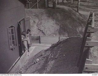 PORT MORESBY, NEW GUINEA. 1943-07-14. CARRIER TERMINAL BUILDING SHOWN FROM THE TOP OF THE REVETMENT SHOWING HEIGHT AND SOLIDITY OF THE PROTECTING WALLS WITH VX124105 STAFF SERGEANT A. J. KIRKMAN ..