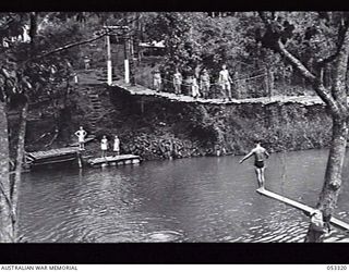 SOGERI VALLEY, NEW GUINEA. 1943-06-26. MIDDAY MESS PARADE OF THE NEW GUINEA FORCE SCHOOL OF SIGNALS CROSSING BRIDGE. BELOW THE BRIDGE CAN BE SEEN DIVING BOARDS AND PONTOONS CONSTRUCTED BY THE ..