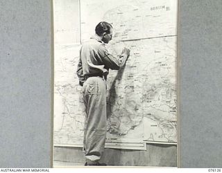 LAE, NEW GUINEA. 1944-09-14. SX3657 CAPTAIN S. GILBERT, AIR INTELLIGENCE LIAISON OFFICER, HEADQUARTERS NEW GUINEA FORCE, EXAMINING POSITIONS ON A MAP IN THE BATTLE ROOM