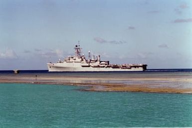 A port beam view of the Third Fleet flagship USS CORONADO (AGF-11) departing Pearl Harbor through the channel.