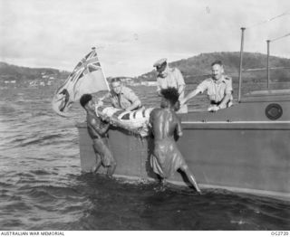 PORT MORESBY, PAPUA. C. 1944. A CASUALTY IN A STOKES LITTER BEING PUT ABOARD A MOTOR LAUNCH OF THE RAAF RESCUE SERVICE WITH THE HELP OF TWO PAPUAN NATIVE CREW MEMBERS