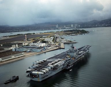 An aerial starboard quarter view of the nuclear-powered aircraft carrier USS ENTERPRISE (CVN 65) as it enters Pearl Harbor. Visible in the background is the USS ARIZONA memorial. Members of the crew man the rail