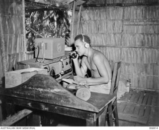 A wireless telegraphist operator, probably Sergeant (Sgt) William 'Billy' Bennett, MM, British Solomon Islands Protectorate Defence Force (BSIPDF), operating an AWA 3BZ teleradio at the Seghe ..