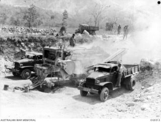 VIVIGANI, GOODENOUGH ISLAND, PAPUA. C. 1943-09. 37603 LEADING AIRCRAFTMAN A. J. WHYTE OF KINBOMBI, QLD, ON TOP OF A STONE CRUSHER OPERATED BY NO. 7 MOBILE WORKS SQUADRON RAAF. CHOKING DUST POURS ..