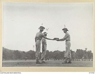 LAE, NEW GUINEA. 1944-06-08. NX7641 CAPTAIN N R WILKINSON (3), PRESENTING THE OLD 2/1ST FIELD WORKSHOP FLAG TO NX34778 LIEUTENANT COLONEL A L M STAINTON, COMMANDING OFFICER, 2/7TH ADVANCED ..