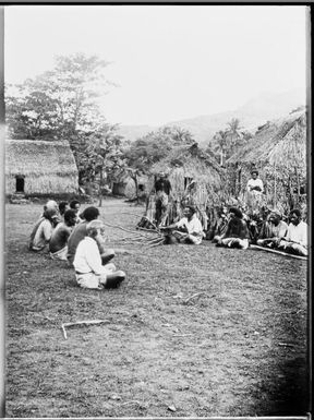 Two groups of seated men, facing each other in a village, Fiji, ca. 1920 / E.W. Searle