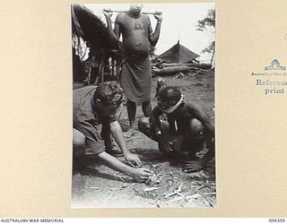 ULUNKOHOITU, NEW GUINEA, 1945-07-18. CPL D.R. MCCLEAN, A COMPANY, 7 PLATOON, 2/6 INFANTRY BATTALION, (1) SHOWING A NATIVE BOY (NICKNAMED "APPLE PIE"), HOW TO DIRECT THE SUN'S RAYS THROUGH A ..