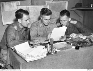 KOROPA, NEW GUINEA. 1944-02-03. VX75606 CAPTAIN H. WATT (1) THE GENERAL STAFF OFFICER III, (AIR), PICTURED STUDYING AERIAL PHOTOGRAPHS AT 7TH DIVISION HEADQUARTERS WITH NGX62 CAPTAIN F.A. JACOBSEN ..