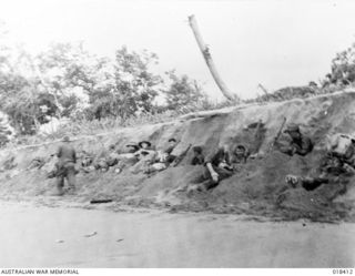Aitape Sector, New Guinea. April 1945. Australian troops advancing along the northern New Guinea Coast take cover under a beach bank, from Japanese shelling
