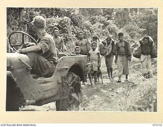 REMPI, NEW GUINEA. 1944-05-09. A MEMBER OF THE 35TH INFANTRY BATTALION PROVIDING TRANSPORT TO NATIVES RETURNING TO THEIR VILLAGES. THE NATIVES ARE EMERGING FROM JUNGLE HIDING IN RESPONSE TO A CALL ..