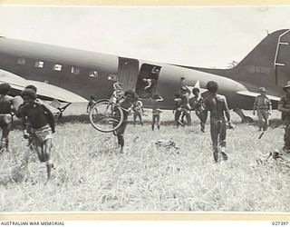 WANIGELA, NEW GUINEA. 1942-10. PAPUAN NATIVES ASSISTING MEN OF THE 2/6TH AUSTRALIAN INDEPENDENT COMPANY TO UNLOAD THEIR EQUIPMENT FROM THE TRANSPORT PLANE IN WHICH THEY HAVE BEEN FLOWN FROM PORT ..