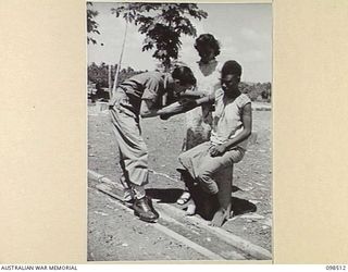 NAMATANAI, NEW IRELAND. 1945-10-29. SERGEANT K. FISHER ASSISTED BY SUGI, THE CHINESE NURSE, TREATING A NATIVE GIRL WITH AN INJECTION FOR YAWS AT THE AUSTRALIAN NEW GUINEA ADMINISTRATIVE UNIT NATIVE ..