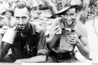NEW GUINEA. SATTELBERG AREA. 3 DECEMBER 1943. PTE. K. BRAWN OF ALBERT PARK, MELBOURNE, VIC., AND PTE. J.K. WRIGHT OF GEELONG, VIC., HAVE A SNACK IN THE FRONT LINE