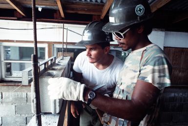 Builder 2nd Class James A. Corter inspects the title work of Jackson Saburo as the two work on a Civic Action Team project at McDonald Memorial Hospital, Palau. The team, composed of United States Navy construction battalion members, is deployed to the island to aid villagers with construction projects and offer vocational training