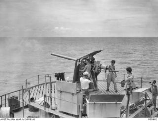 AT SEA BETWEEN FINSCHHAFEN, NEW GUINEA AND BIAK. 1945-04-04. THE 12 PR GUN MOUNTED ON THE STERN OF THE VAN HEUTSZ IS FIRED BY US ARMY GUNNERS DURING A PRACTICE ALERT