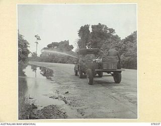 TOROKINA, BOUGAINVILLE ISLAND. 1945-01-17. NX120943 CORPORAL W.G. JONES, 2/1ST MALARIAL CONTROL UNIT AND HIS TWO NATIVE HELPERS OPERATING A PRESSURE TANK FROM A JEEP TRAILER WHILE SPRAYING AREAS OF ..