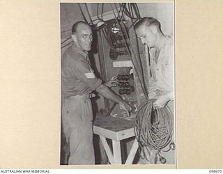 TOROKINA, BOUGAINVILLE. 1945-11-09. SERGEANT A.J. MUNRO, ELECTRICIAN, KOOKAROOS CONCERT PARTY (1) STANDING BY HIS SWITCHBOARD READY TO CONTROL LIGHTING EFFECTS WHILE TECHNICIANS CORPORAL E.J. ..