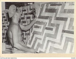 TOROKINA, BOUGAINVILLE. 1945-05-31. SAPPER R. BANKS, 10 FIELD COMPANY ROYAL AUSTRALIAN ENGINEERS, FITTING A BAMBOO SCREEN INTO PLACE ON THE OUTER WALL OF GLOUCESTER HOUSE AT HEADQUARTERS 2 CORPS ..