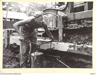 BOUGAINVILLE, 1945-07-16. SAPPER H. BISH, 6 MECHANICAL EQUIPMENT COMPANY, ATTACHED 3 DIVISION, USING A VOLUME GUN TO GREASE THE TRACK BEARINGS OF A BULLDOZER. HE IS WORKING ON THE BUIN ROAD EAST OF ..