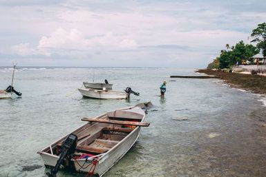 Man standing in the sea with boats, Nukunonu, Tokelau