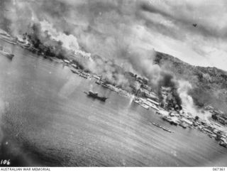 RABAUL, NEW BRITAIN, 1943-11-02. AERIAL PHOTOGRAPH OF THE TOWN ABLAZE DURING AN ATTACK BY MITCHELL AIRCRAFT OF THE U.S. FIFTH AIR FORCE. A MITCHELL CAN BE SEEN THROUGH THE SMOKE AT TOP LEFT