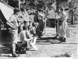 ON TADJI AIRSTRIP RAAF KITTYHAWK PILOTS BEING BRIEFED BY CONGO KINNINMONT (IN HAT) THE COMMANDING OFFICER OF NO. 75 SQUADRON RAAF BEFORE GOING OUT TO PROVIDE TOP COVER FOR BOMBER AIRCRAFT ATTACKING ..