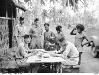 MILNE BAY, PAPUA. C. 1943-08. NEW GUINEA NATIVES STOP WORK TO LOOK ON WHILE SQUADRON LEADER ARCHIE MACARTHUR RAAF OF BAIRNSDALE, VIC, RECORDS THE FIRST SERVICE VOTE FOR THAT AREA IN THE AUSTRALIAN ..