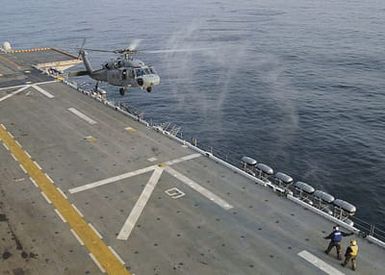 A US Navy (USN) MH-60S Seahawk helicopter is directed onto the flight deck aboard the USN Tarawa Class Amphibious Assault Ship, USS SAIPAN (LHA 2). The helicopter is performing "touch and go" training in order for the squadron and the ship to meet qualification standards to maintain deployment readiness