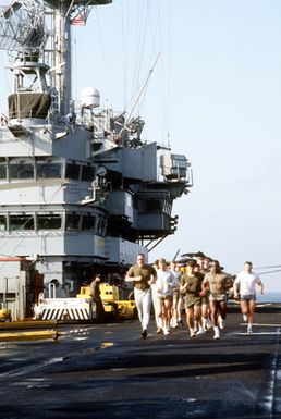 Marines run on the flight deck of the amphibious assault ship USS GUAM (LPH-9) during morning physical training (PT)