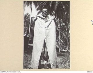 AITAPE, NEW GUINEA. 1945-04-10. CORPORAL P. PHILLIPS AT HEADQUARTERS 6 DIVISION HOLDING AN OUTSIZE PAIR OF ARMY TROUSERS