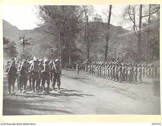 RABAUL, NEW BRITAIN. 1945-10-01. JAPANESE SOLDIERS WITH PICKS AND SHOVELS ON THEIR WAY TO WORK PASS TROOPS OF HEADQUARTERS 11 DIVISION ON PARADE