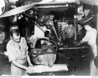 New Guinea. 1944. The press being prepared to print copies of "Guinea Gold" the newspaper distributed daily to troops in New Guinea. Shown, Private G. Spencer of Bowen, Qld, native boy Seri Eno, ..