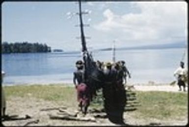 Men carrying canoe to sea; matching red skirt and headress