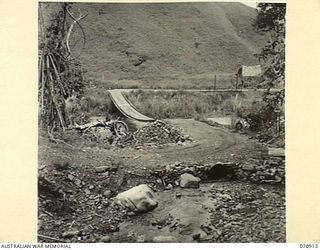 WAU - LAE ROAD, NEW GUINEA, 1944-02-26. THE ROAD IS 35 MILES FROM WAU, CROSSING A CULVERT AND SUSPENSION BRIDGE OVER THE SNAKE RIVER. THE ROAD AT THIS POINT IS MAINTAINED BY THE 1ST MECHANICAL ..