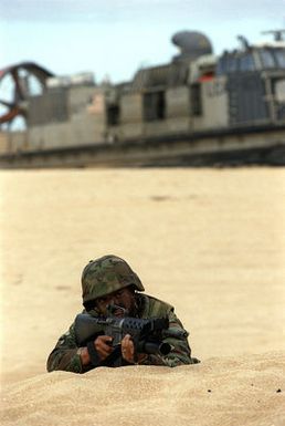 US Marine Corps LCPL Donald Retreage of Co. A, 1ST Light Armored Reconnaissance, Camp Pendleton, California, waits for the signal to move forward from his perimeter position during exercise RIMPAC '98 beach assault. Behind him is a Landing Craft, Air Cushion vehicle bringing more Marines to the beach