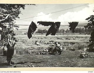 DALLMAN RIVER, NEW GUINEA, 1944-02-21. NX124592 PRIVATE A. KENDALL (1), STANDS GUARD WHILE NX124527 PRIVATE V. DEVONSHIRE (2) LIGHTS THE FIRE AT THE "SHANTY TOWN", CAMP OF THE 30TH INFANTRY ..