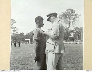 LAE, NEW GUINEA. 1944-09-12. VX13 LIEUTENANT GENERAL S.G. SAVIGE, CB, CBE, DSO, MC, ED, GOC NEW GUINEA FORCE, PRESENTING THE BRITISH EMPIRE MEDAL, (CIVIL DIVISION), TO GOMERI. THE CITATION TO THE ..