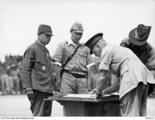 CAPE WOM, NEW GUINEA, 1945-09-13. MAJ-GEN H.C.H. ROBERTSON, GOC 6 DIVISION, SIGNING THE INSTRUMENT OF SURRENDER. LT-GEN H. ADACHI, COMD 18 JAPANESE ARMY IN NEW GUINEA, FORMALLY SURRENDERED TO ..