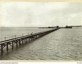 PORT MORESBY, PAPUA, 1944-03-21. THE EMPIRE SILVER, AN OIL TANKER BERTHED ON THE END OF THE WHARF, VIEWED FROM A HILL. THE PIPELINES RUNNING BESIDE THE PATHWAY AT THE WHARF ARE CONTROLLED BY THE ..