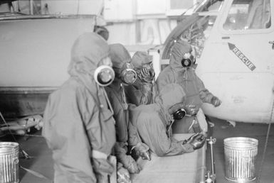 Crew members wearing nuclear, biological and chemical warfare gear stand by while participating in a"casualty"evacuation drill aboard the amphibious assault ship USS GUAM (LPH 9) during the field training Exercise SOLID SHIELD'87