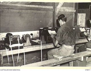 LAE, NEW GUINEA. 1945-02-06. SX24782 LANCE CORPORAL D.K. WALKER (1) AND NX15117 SIGNALLER W.E. BALL (2, PART OBSCURED) OPERATING THE PUNCHING MACHINES OF THE WHEATSTONE EQUIPMENT AT THE SIGNALS ..