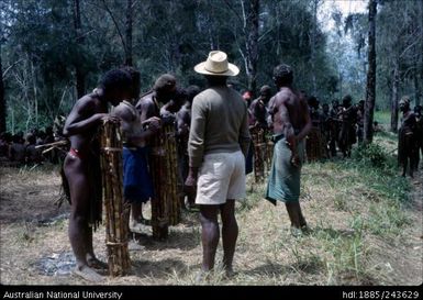 Men lined up, holding traditional items