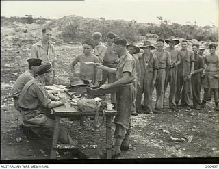 VIVIGANI, GOODENOUGH ISLAND, PAPUA. 1943-12-26. PAY PARADE FOR AIRMEN OF NO. 30 (BEAUFIGHTER) SQUADRON RAAF. THE OFFICERS AT THE DESK IN THE OUTDOORS ARE PILOT OFFICER R. J. M. WALKER OF CAULFIELD, ..