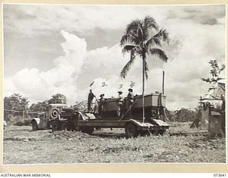 LAE, NEW GUINEA. 1944-05-28. A MOTOR LAUNCH BEING TRANSPORTED BY TANK TRAILER FROM 5TH COMMANDER ROYAL ENGINEERS, (AIF), TO THE WATERFRONT FOR LAUNCHING. MEMBERS OF THE 2ND MARINE FOOD SUPPLY ..