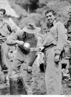 EORA CREEK, PAPUA. C. 1942-09-02. PRIVATE W. PARR IS HELPED TO A CUP OF TEA BY PRIVATE H. BRADBURY AFTER A CLASH WITH JAPANESE JUNGLE FIGHTERS IN THE KOKODA AREA. BOTH MEN ARE FROM THE 39TH ..