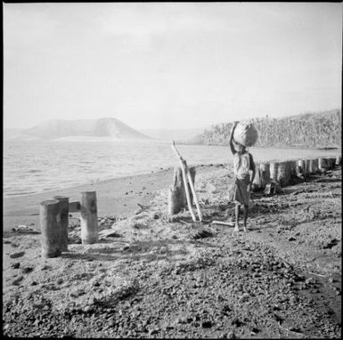 Remains of a jetty with a woman carrying a loaded bag on her head, Rabaul Harbour, New Guinea, 1937 / Sarah Chinnery