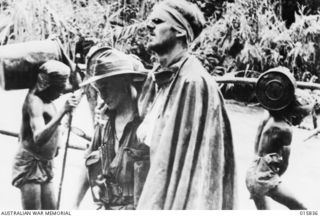 During the advance on Salamaua VX89711 Sergeant Gordon Raymond Charles Ayre MM, a 58/59th Battalion bandsman from Shepparton, Victoria, in pouring rain assists a wounded mate, VX132355 Private ..