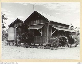 BULOLO, NEW GUINEA. 1945-10-17. THE FRUIT PLANTATION OPERATED BY MEMBERS OF 5 INDEPENDENT FARM PLATOON IS AT BULOLO. CORPORAL A.L. DAVY IS SHOWN STANDING IN FRONT OF THE PLANTATION HOUSE